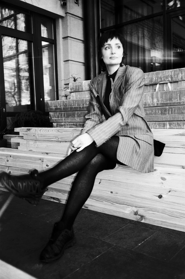 Oksana Hoshva sitting on wooden steps near a building, black-and-white photo